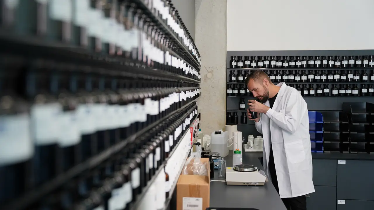 Our perfumer in the lab in front of the shelf wall of fragrance raw materials
